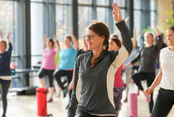 Eine Frau in Sportkleidung hebt die Hand, im Hintergrund sind weitere Personen.