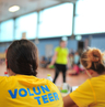 Mehrere Personen sitzen in einem gelben Volunteer-Shirt an einem Tisch.