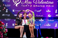 Zwei Gymnastinnen sitzen links und rechts von ihrer Trainerin und bilden mit ihren Armen ein Herz