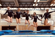 5 Turnerinnen springen auf einem Trampolin in die Luft.