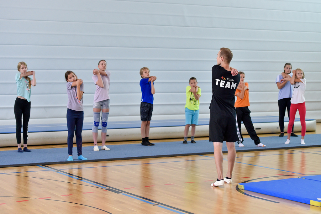 Ein Mann macht mit Kindern eine Dehnübung in der Turnhalle.