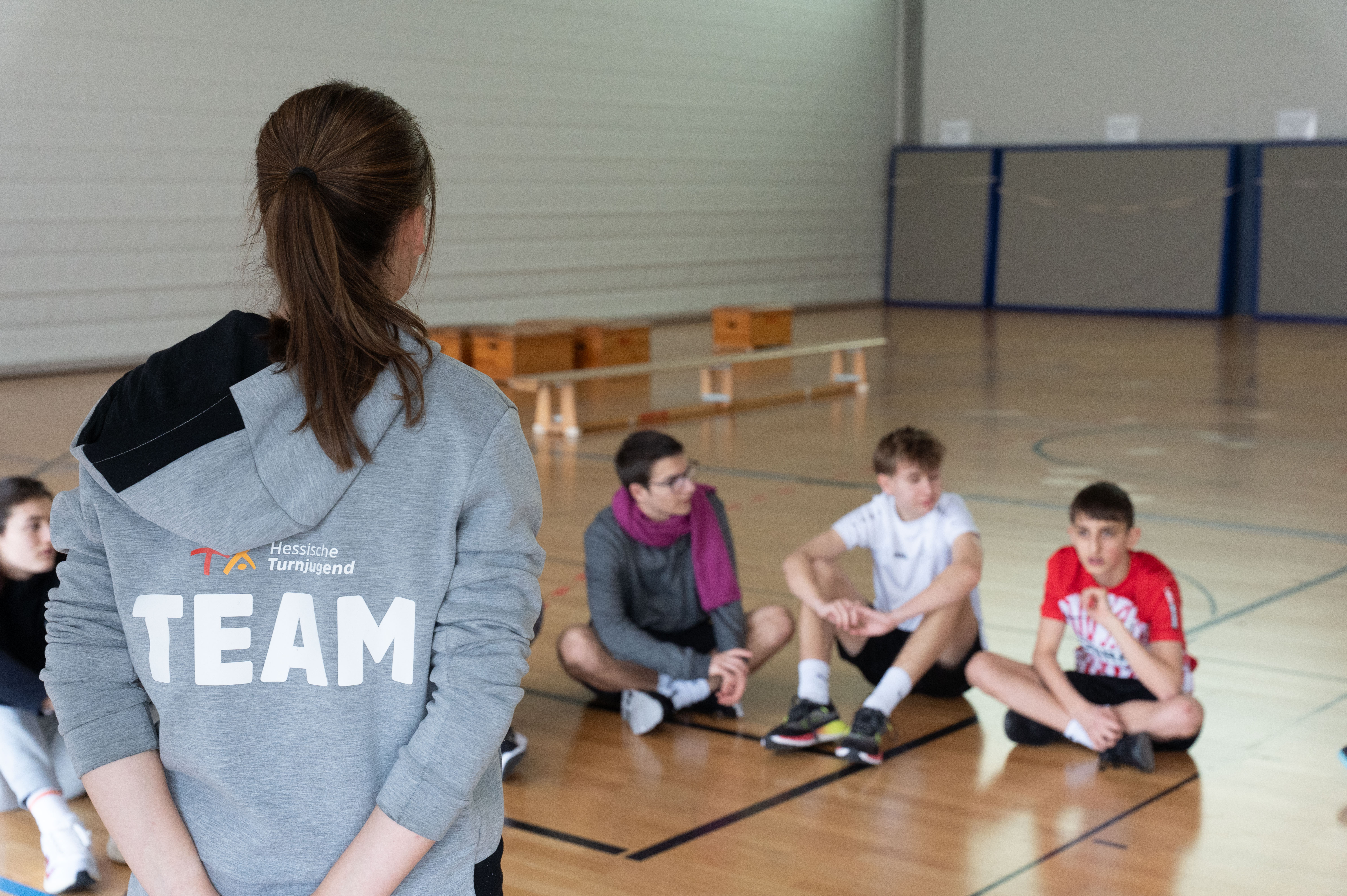 Eine junge Frau erklärt Schülern etwas in der Sporthalle.