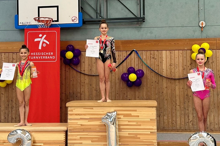 Turnerinnen der Rhythmischen Sportgymnastik stehen auf dem Treppchen und halten ihre Auszeichnungen. 