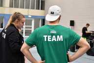 Ein Mann steht in einer Sportgalle und träft die Rückenaufschrift "TEAM".