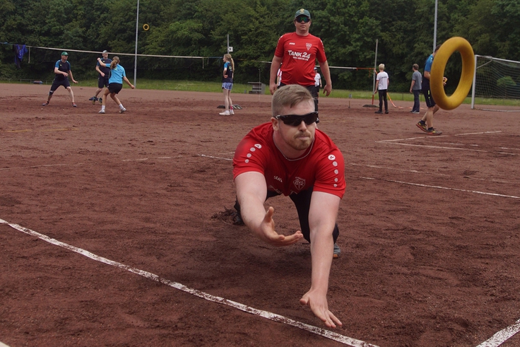 Ein Mann wirft sich auf einem Spielfeld nach einem Tennisring.