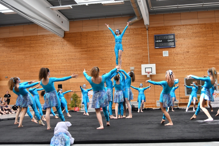 Eine Showgruppe in blauen Kostümen zeigt eine Choreographie mit Hebefigur.